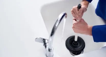 A person plunging a white kitchen sink, with water running from the faucet